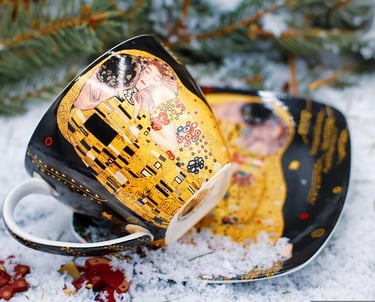 aza de café y plato con el estampado de la pintura "El Beso" de Gustav Klimt, colocados sobre nieve 