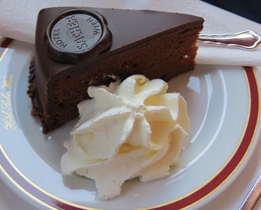 Porción de tarta Sacher con su sello oficial de chocolate y una guarnición de nata montada