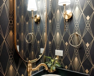 Baño elegante con papel tapiz geométrico, espejo redondo, luminarias doradas y grifería de lujo.