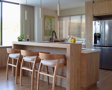 Cocina moderna con acabados en madera clara, isla central y sillas de diseño escandinavo.