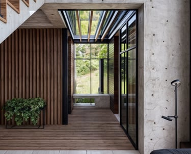 Pasillo moderno con concreto y madera, rodeado de naturaleza.
