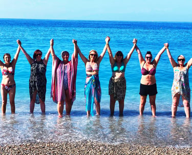 A grour of women in swimwear, raising arms and holding hands in the sea