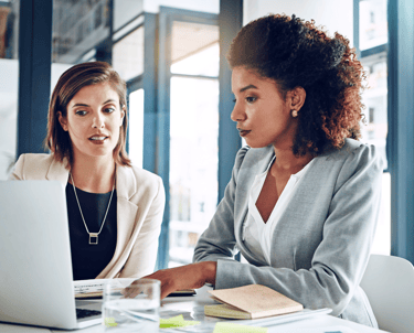 duas mulheres, vestindo roupa social, trabalhando em um escritório.