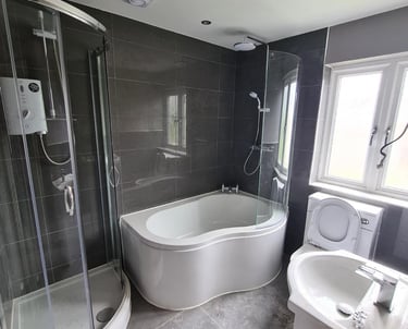 Modern bathroom featuring a corner shower enclosure, P-shaped bathtub, and grey tile walls.
