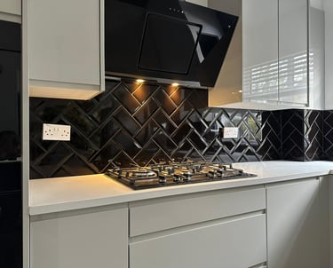 Modern white kitchen featuring a black glass herringbone tile backsplash and gas stovetop.