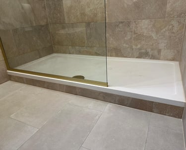 Walk-in shower with a low-profile white tray, glass enclosure, and beige stone wall tiles.