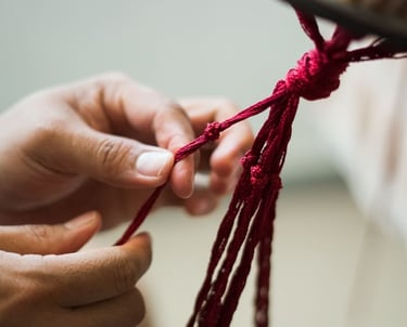 Manos realizando una pieza de macramé colgante en color rojo.