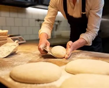 Persona sosteniendo una pieza de pan crudo para llevarla al horno