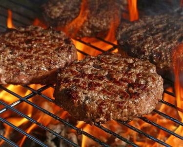 Fresh hamburgers grilling on-site at a backyard BBQ with perfect grill marks and flames