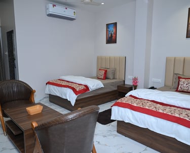 Modern hotel room with twin beds, red decorative runners, and a seating area with leather chairs.