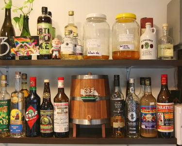Rustic home bar shelf featuring a wooden barrel and various bottles of Brazilian cachaça and spirits.