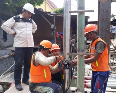 Construction workers in safety gear installing a submersible water pump at an outdoor site.