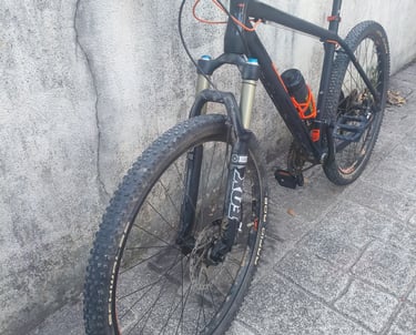 Bicicleta de montanha KTM preta e laranja com suspensão dianteira em destaque, vista frontal em três