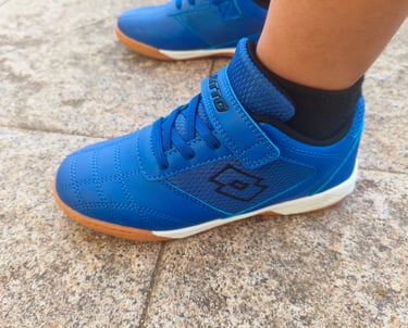 Criança a usar sapatilha infantil Lotto azul com velcro e sola laranja num chão de calçada