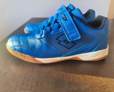 Sapatilha infantil Lotto azul com velcro e sola laranja vista de lado numa mesa de madeira