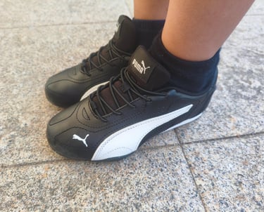 Criança a usar as sapatilhas infantis Puma Catch pretas e brancas num chão de calçada