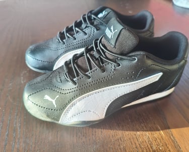 Sapatilhas infantis Puma Catch pretas e brancas vistas de lado em cima de uma mesa de madeira