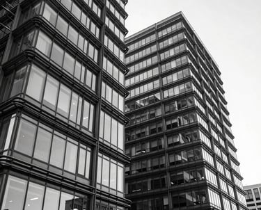 A high-contrast black and white photograph of modern office architecture, conveying a professional and dynamic atmosphere. Steel blue accents.