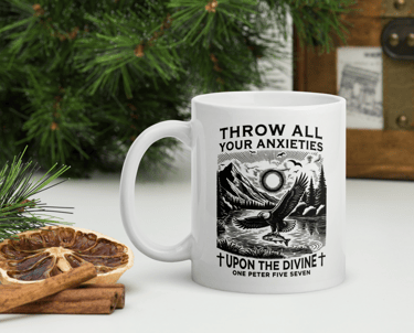 White ceramic coffee mug with a religious graphic featuring an eagle and mountain landscape next to cinnamon sticks.