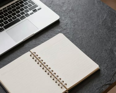Overhead view of a minimalist workspace with a sleek laptop and a notepad. Soft natural light, slate and off white palette, North American / International office setting.