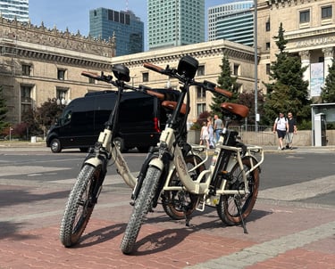 Two cream electric folding bikes with fat tires parked on a city street in Warsaw near modern skyscrapers.