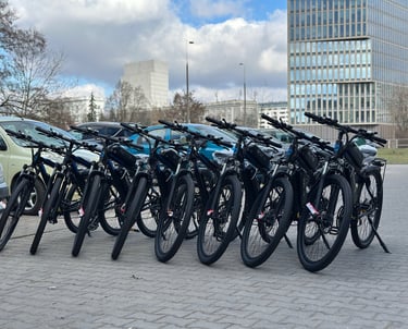 A row of black electric mountain bikes parked on a city street near modern office buildings.