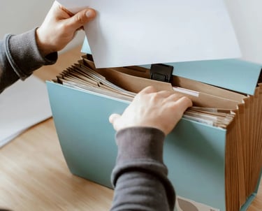 A person organizing documents in a blue accordion expanding file folder on a wooden desk.