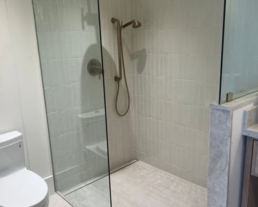 Modern walk-in shower with vertical subway tiles, glass door, and brushed gold rain shower head.