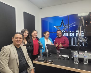 A group of five smiling professionals posing in a modern radio broadcasting studio with microphones and digital displays.