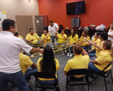A group of workers in yellow shirts participating in a collaborative team building exercise with yellow ropes.