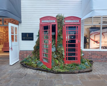 Red British telephone boxes filled with lush green plants and moss in a floral outdoor display.