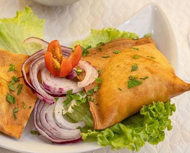 Golden fried vegetable samosas served on a plate with fresh lettuce, red onions, and cherry tomatoes.