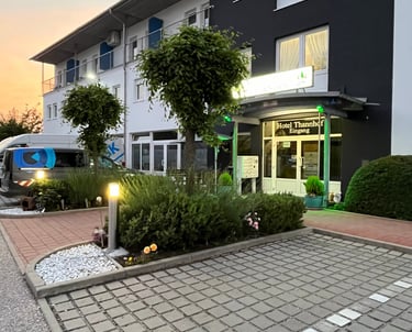 The exterior entrance of Hotel Thannhof at sunset with a paved parking area and green landscaping.