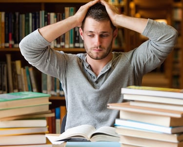 Studente con le mani tra i capelli in segno di frustrazione; intorno libri aperti e chiusi