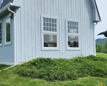 A light blue gambrel roof barn conversion home with white windows and a green lawn with dandelions.