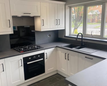 A simple kitchen with white cabinets and grey worktops.