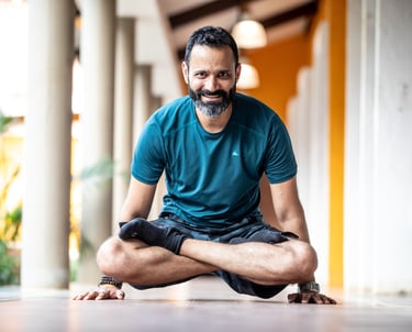 Smiling yoga instructor performing an advanced arm balance pose in a bright studio hallway.