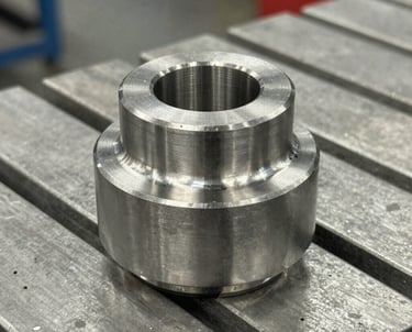 Precision machined stainless steel industrial component on a metal workbench in a CNC shop.