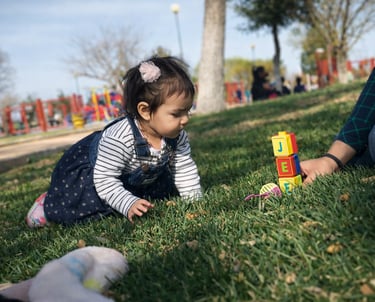 Una niña pequeña jugando con bloques de letras de colores sobre el césped en un parque