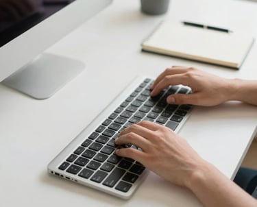 Photography of a clean, minimalist North American desk focused on hands typing on a modern keyboard next to a notebook. The scene is bright and conveys a sense of organized productivity and security.