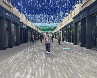 A person walks through an outdoor shopping mall under a blue hanging ribbon art installation.