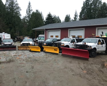5 trucks with plows are parked in front of a 3 bay shop. The trucks are in a semi circle facing the camera