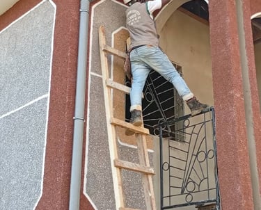 A construction worker on a wooden ladder installs a gutter drainage system on a building.