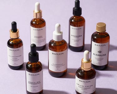 Photography of high-end skincare bottles arranged artistically on a light lilac textured surface. South American / Brazilian brand aesthetic.