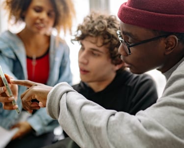 Diverse students collaborating and looking at a smartphone screen together in a classroom.