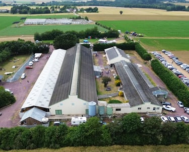Vue aérienne d'un événement agricole avec de grandes granges industrielles, un parking et des champs