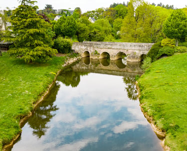 Vue aérienne d'un vieux pont en arc de pierre enjambant une rivière calme, entouré d'une végétation 