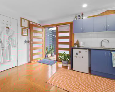 Kitchenette at Marche Home Stay with blue cabinets, a small fridge, bathrobes, and doors opening to a cosy outdoor area.