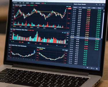 A detailed photograph of a professional trading dashboard on a laptop, featuring complex charts and data tables. North American / Global Financial Market.