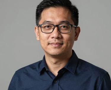 Portrait of a Southeast Asian man with glasses, looking professional and friendly, dressed in a simple navy blue shirt against a neutral background.